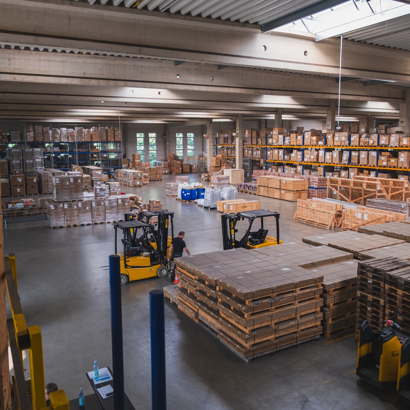Blick von oben in die Lagerhalle mit Staplern und Paletten